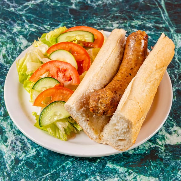 Mugsy's Hideout Italian sausage sandwich with a side salad on a white plate.