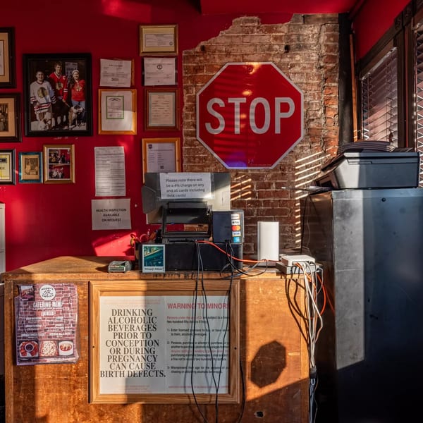 A red wall with framed photos and certificates, a stop sign, and a wooden counter with a POS system.