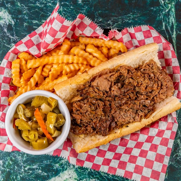 Italian beef sandwich with crinkle-cut fries and a side of giardiniera in a red checkered basket.