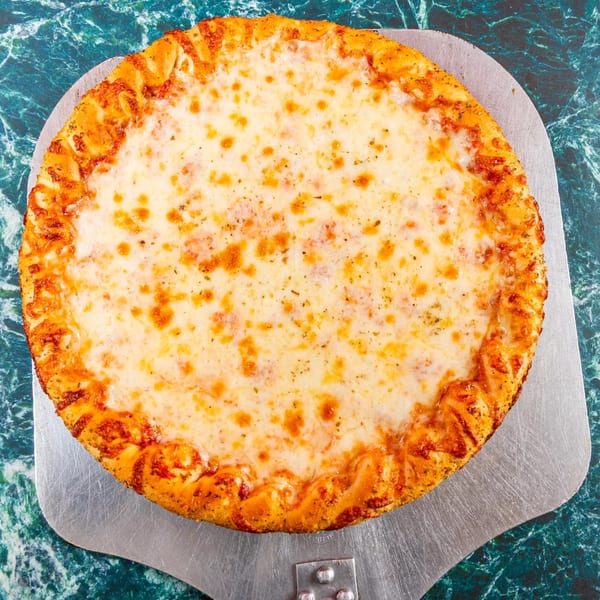 A round, cheesy pizza with a golden crust sits on a metal pizza peel against a green marble background.