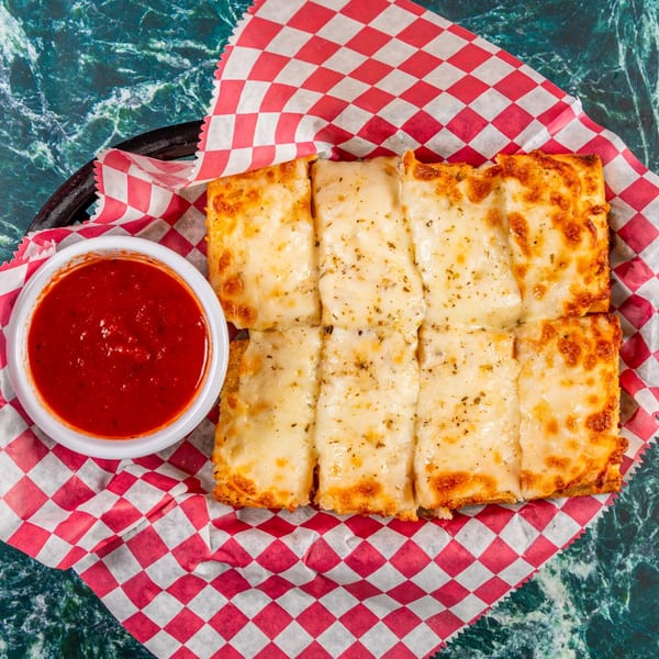 Cheesy garlic breadsticks with herbs and a side of marinara sauce on red and white checkered paper.