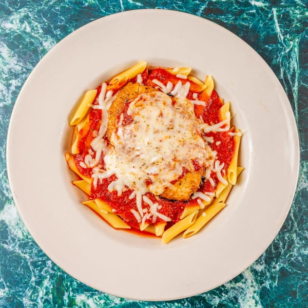 Chicken Parmesan with penne pasta and marinara sauce, topped with melted mozzarella cheese.