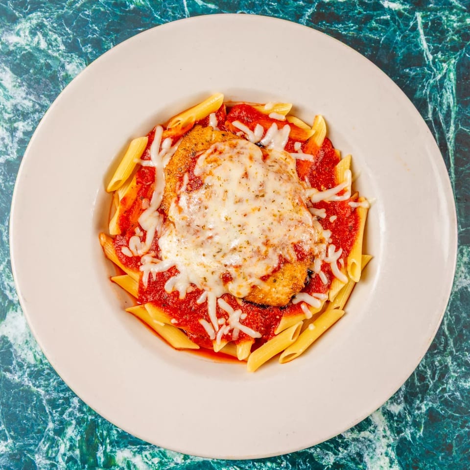 Chicken Parmesan with penne pasta and marinara sauce, topped with melted mozzarella cheese.