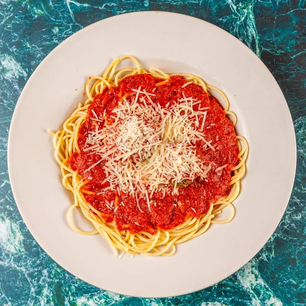 Spaghetti with red marinara sauce and a generous topping of shredded Parmesan cheese on a white plate.
