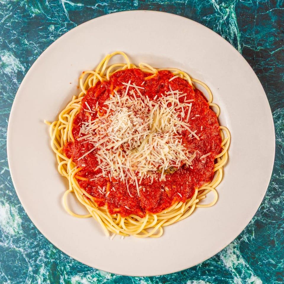 Spaghetti with red marinara sauce and a generous topping of shredded Parmesan cheese on a white plate.