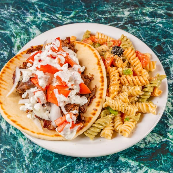 A gyro with meat, tomatoes, onions, and white sauce, served with a side of pasta salad.