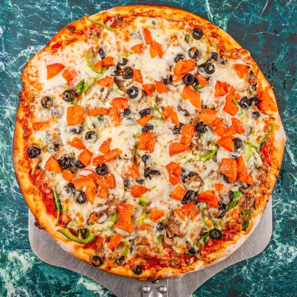 Mugsy's Hideout's Italian pizza, topped with tomatoes, olives, green peppers, and mushrooms, on a pizza peel.