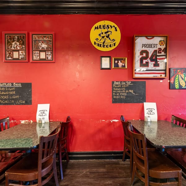Interior of Mugsy's Hideout with red walls, sports memorabilia, and two tables with chairs.