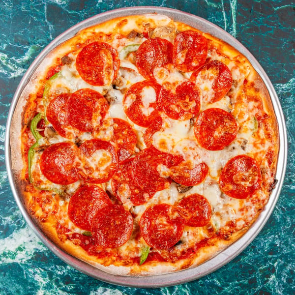A whole pepperoni pizza with melted cheese, green peppers, and mushrooms on a metal pan.