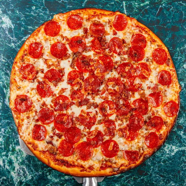 Mugsy's Hideout pepperoni and sausage pizza on a dark green marble surface.
